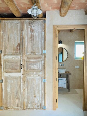 Ein rustikales Badezimmer mit Holztür, rundem Spiegel und weißem Waschbecken.