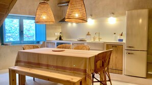 A kitchen with a dining table, chairs, and a bench. There are hanging lights and a refrigerator. - Restored fisherman's house in l'Escala (L'Escala)
