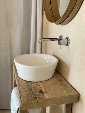 Ein weißes Keramikbecken auf einem Holzregal mit einem Chrom-Wasserhahn.
