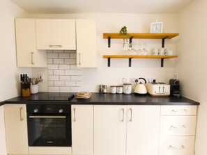 Eine Küche mit weißen Schränken, einer schwarzen Arbeitsplatte und einem Bosch-Backofen. Darüber befinden sich Regale mit Tassen und einer Pflanze.