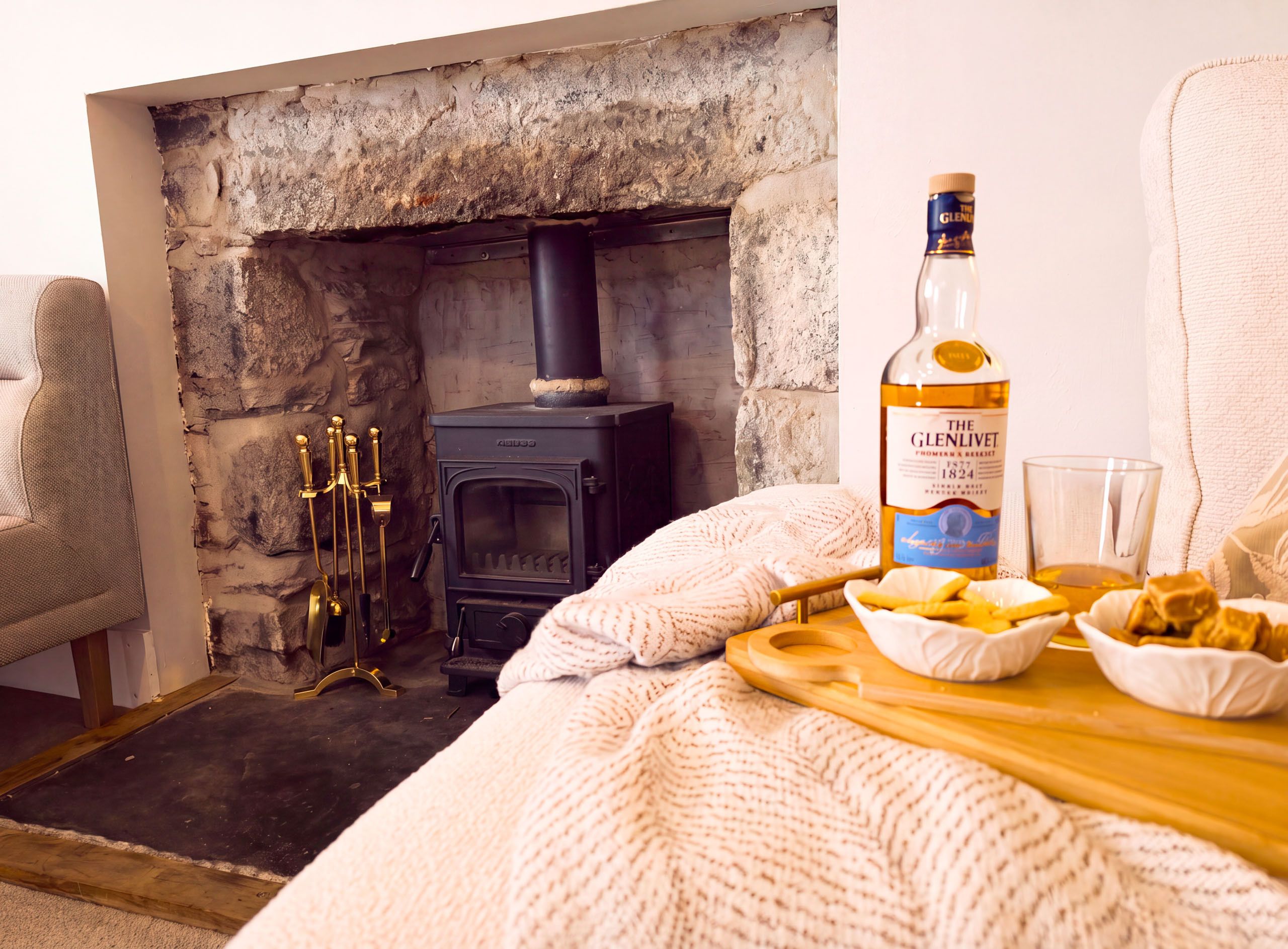 A cozy room with a stone fireplace, a bottle of The Glenlivet whiskey, and a tray with snacks.