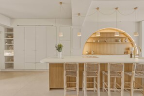 A modern kitchen with a central island, bar stools, pendant lighting, and a wooden accent wall. - Villa Ti Bassin Arcachon - Waterfront, right on the water (Arcachon)