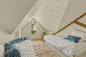 Ein Schlafzimmer mit schrägverdeckter Decke, zwei Betten, einem Fenster und Holzbalken.