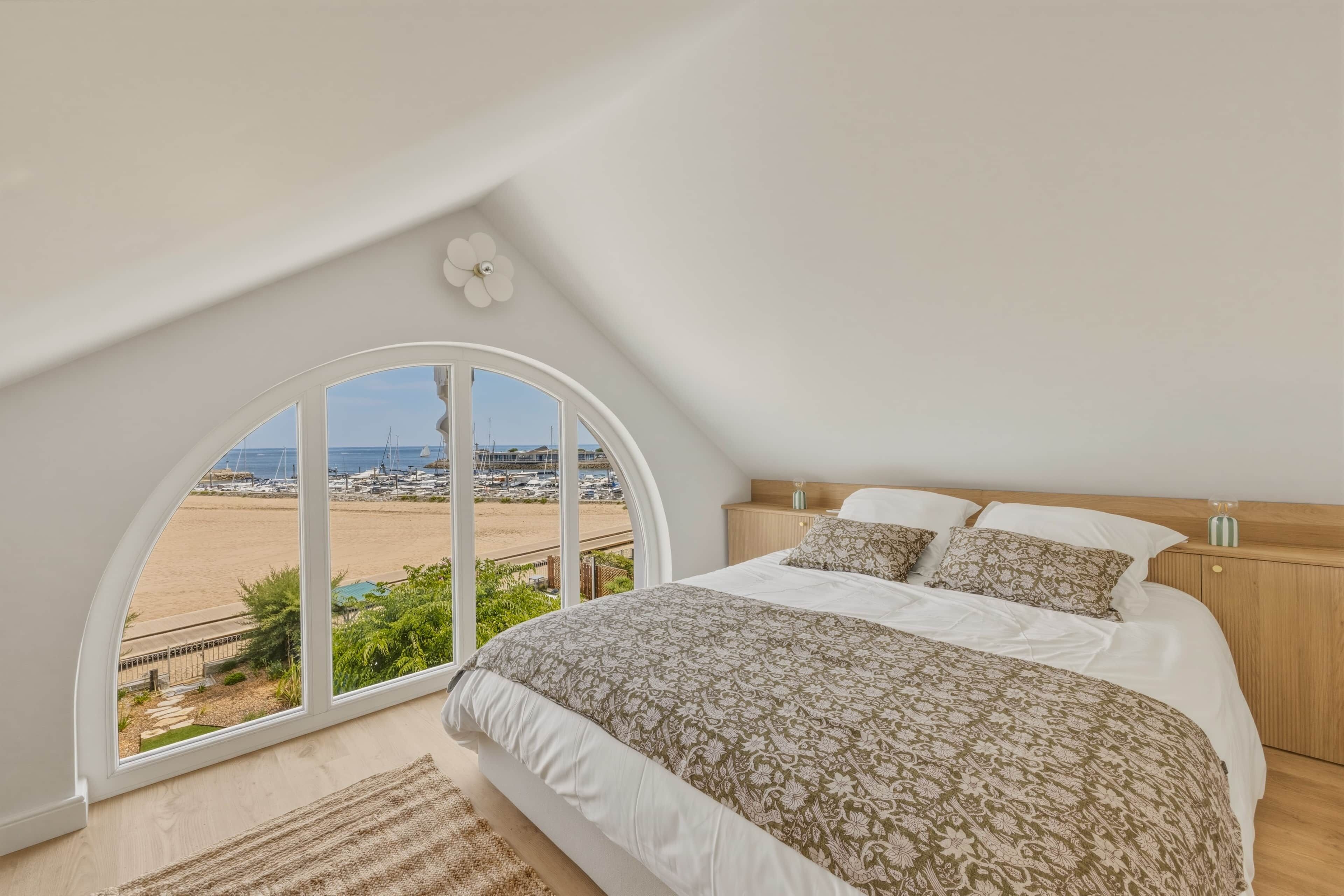 A bedroom with a large arched window, a bed with patterned bedding, and a wooden headboard.