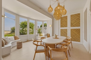 A spacious room with a large dining table surrounded by chairs, a seating area with a bench, and large windows offering a view of greenery and a beach. - Villa Ti Bassin Arcachon - Waterfront, right on the water (Arcachon)