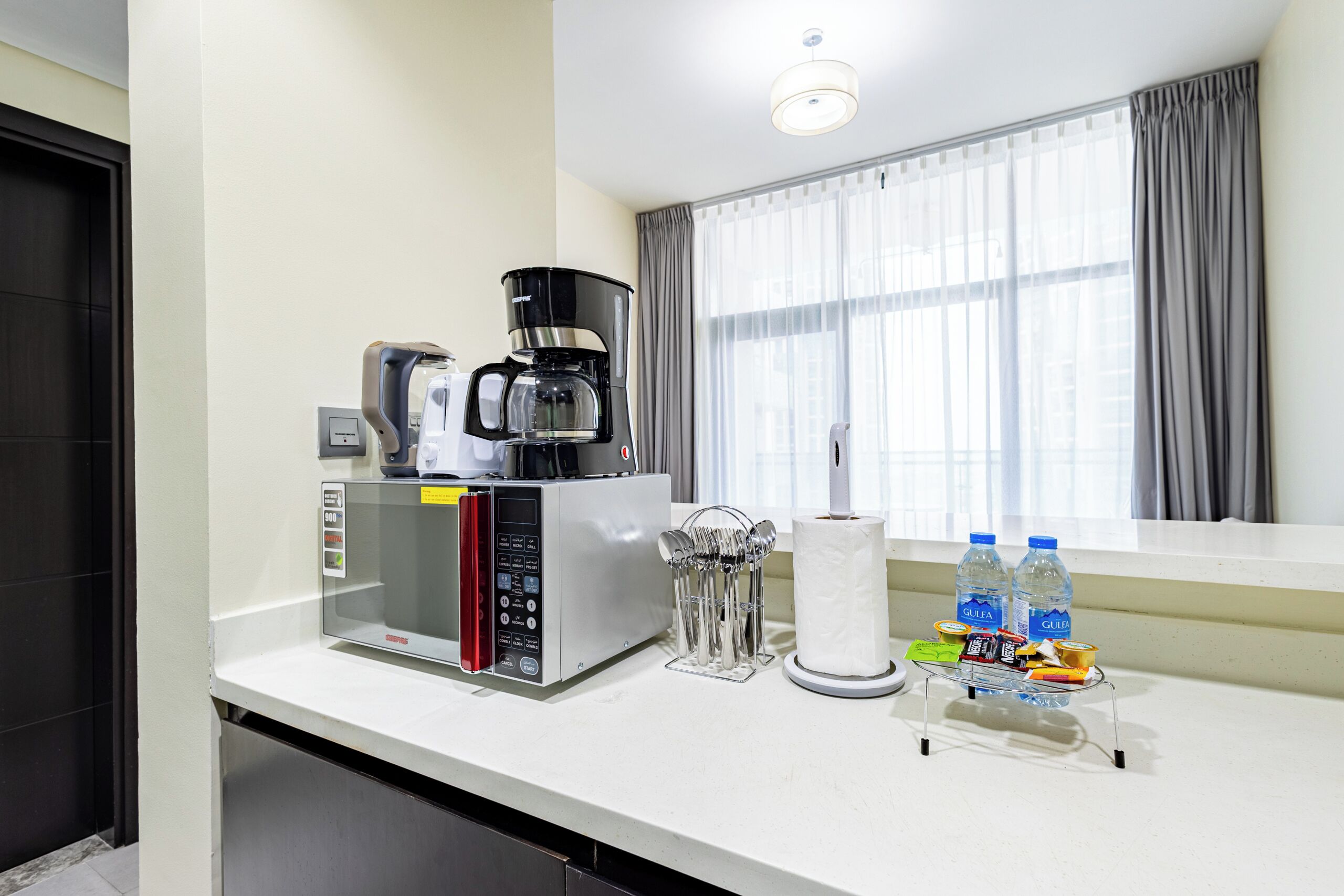 Une petite cuisine équipée d’une machine à café, d’un porte-essuie-tout et de bouteilles d’eau.