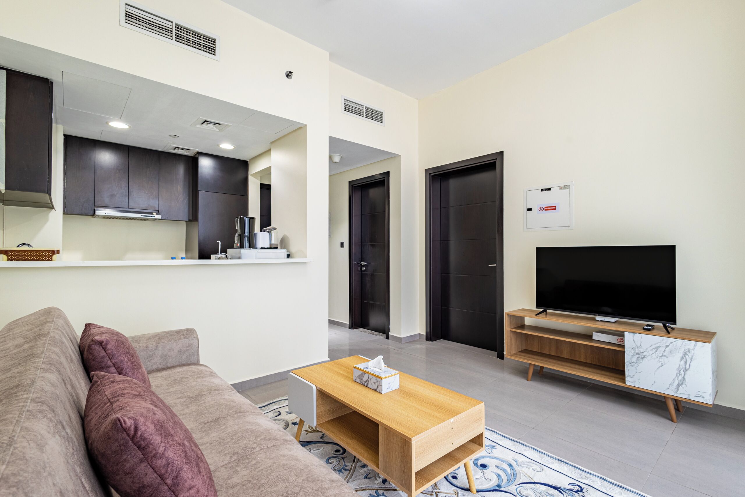 A modern living room with a sofa, coffee table, TV, and kitchen area.