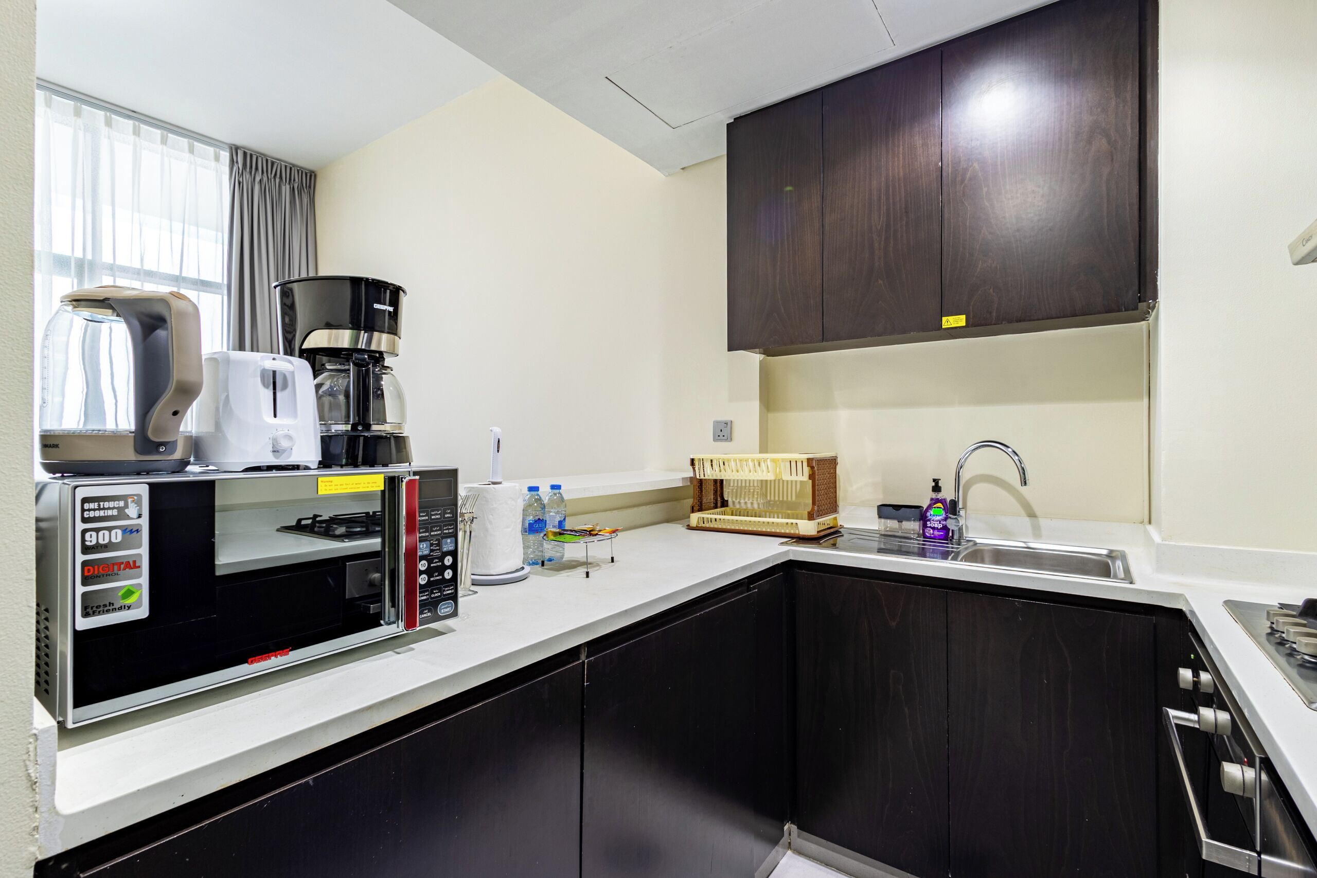 Cocina compacta con cafetera, microondas, tostadora, lavabo y un armario.