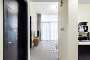 Habitació d'hotel amb un armari de fusta fosca, una taula de fusta petita amb un televisor de pantalla plana, una finestra gran amb cortines lleugeres i una cuineta amb cafetera i fogó.