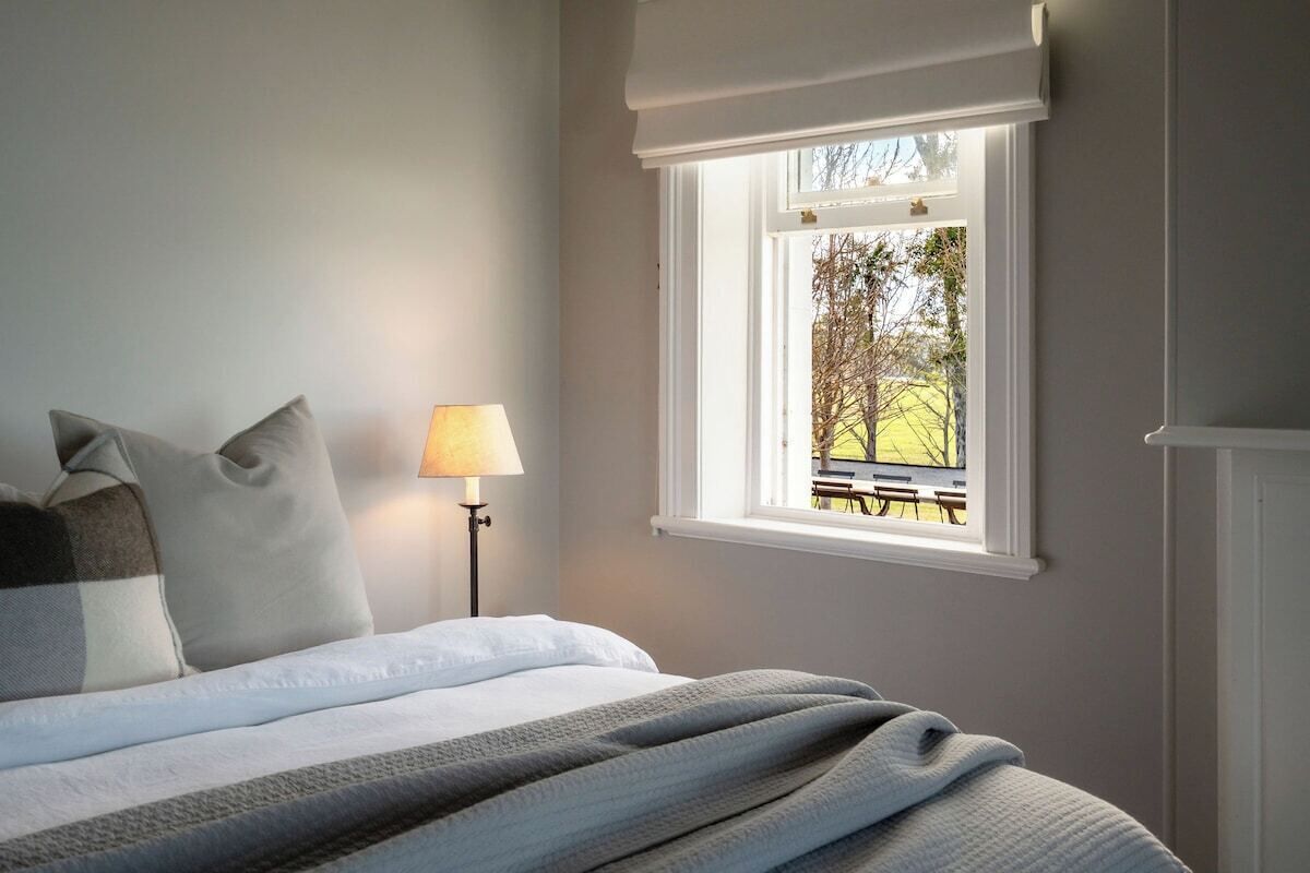 Une chambre à coucher avec un lit, des oreillers, une lampe et une fenêtre donnant sur un espace extérieur.