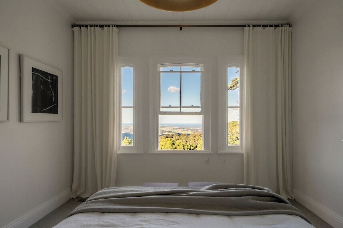Une chambre à coucher avec un lit, une fenêtre avec des rideaux et un tableau encadré accroché au mur.