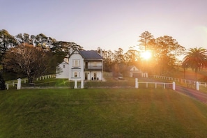 A two-story white house with a balcony, surrounded by a white fence, set against a backdrop of trees and a clear sky. - 'Glenworth House' - Heritage Berry Mountain Estate (Berry Mountain)