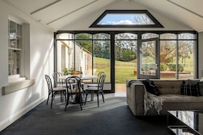 Ein Wintergarten mit Glastür zum Garten, ein Esstisch mit Stühlen und eine Couch.