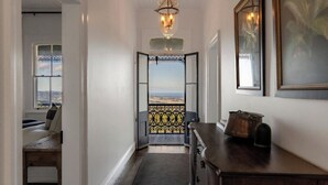 Um corredor com vista para o exterior, um candelabro, um banco e uma cômoda.