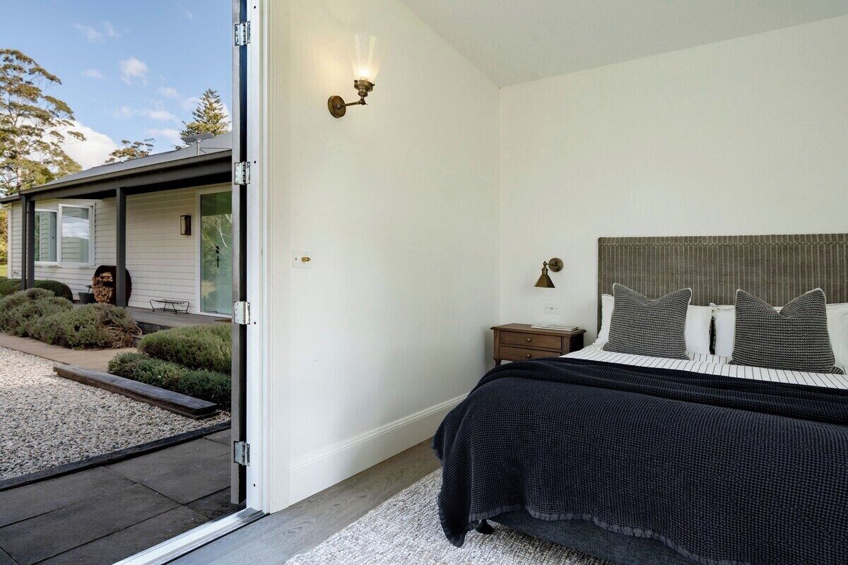 Une chambre à coucher avec un lit, une table de chevet, une lampe et une vue sur une maison à l’extérieur.