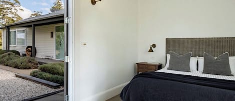 Et soveværelse med seng, et natbord, en lampe og udsigt til et hus udefra.