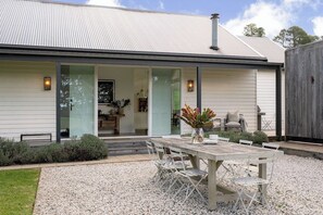A modern house with a covered patio, a dining area with a table and chairs, and a visible kitchen area. - 'The Cottage' at Glenworth Estate (Berry Mountain)
