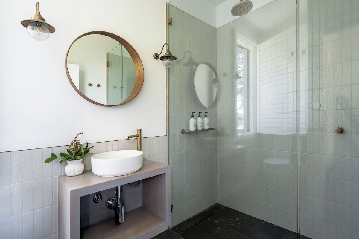 A modern bathroom with a round mirror, a white sink, and a glass-enclosed shower.