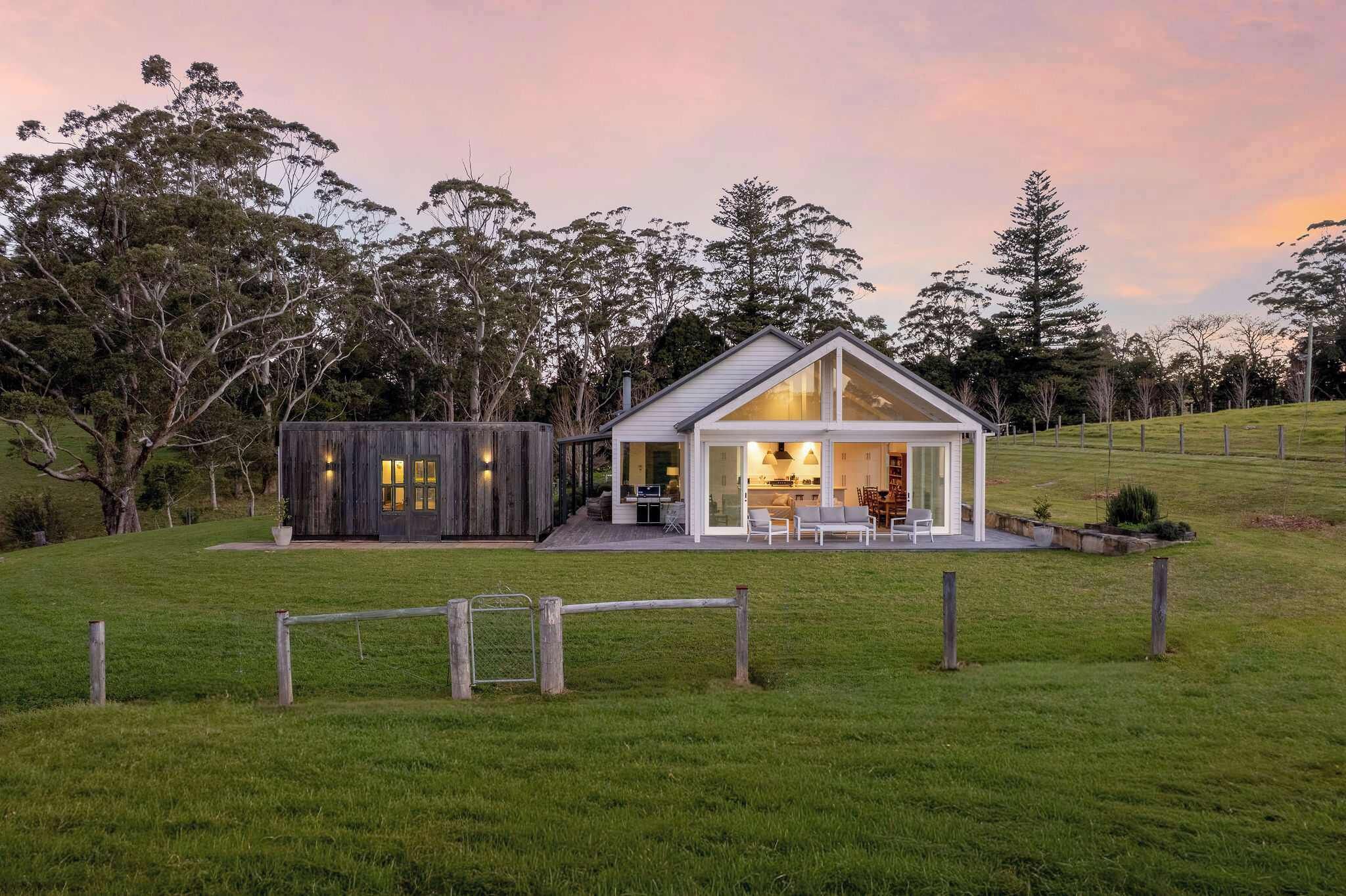 A modern house with a large glass door and a smaller wooden structure in a grassy field.
