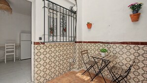 Eine kleine Terrasse im Freien mit einem Metalltisch und -stühlen, einer weißen Tür und wandbündigen, gemusterten Fliesen.
