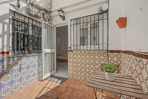 A small patio with a wooden table, a potted plant, and a door leading to a room with patterned tiles. - ‘El Olivo 1’ Apartment with Private Terrace, Wi-Fi, and Air Conditioning (Málaga)