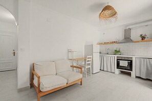 Eine moderne Küche mit weißen Schränken, eine Essecke mit Holztisch und -stühlen sowie ein Sofa.