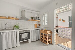 A kitchen with white tiles, a stove, a microwave, and a wooden shelf. - ‘El Olivo 1’ Apartment with Private Terrace, Wi-Fi, and Air Conditioning (Málaga)