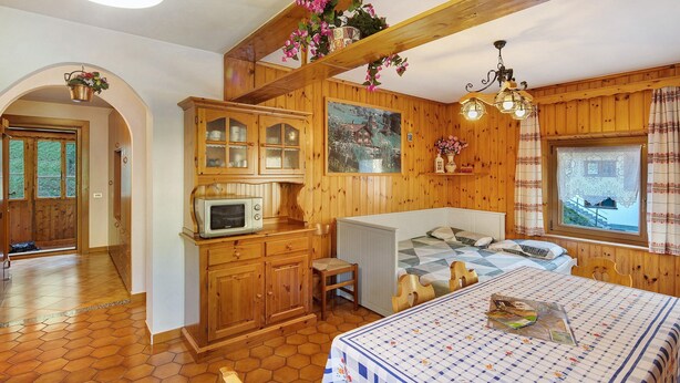Una habitación acogedora con una cama, una mesita, un microondas y armarios de madera.