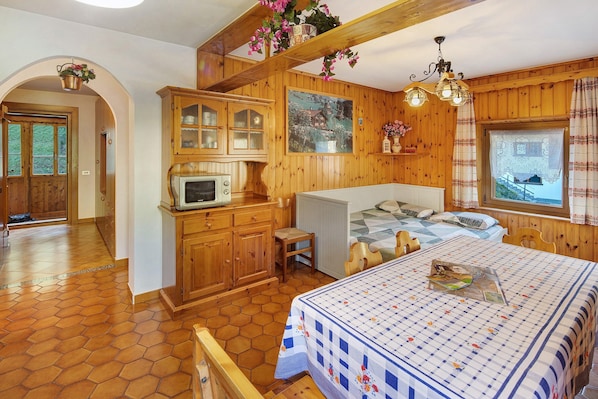 A cozy room with a bed, a small table, a microwave, and wooden cabinets.