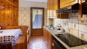Una cocina con armarios de madera, estufa, fregadero y una mesa de comedor con mantel a cuadros.