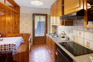 A kitchen with wooden cabinets, a stove, a sink, and a dining table with a checkered tablecloth.