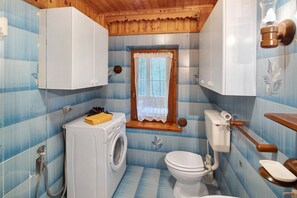 Un bany compacte amb rentadora, vàter i finestra amb cortines de gallet.