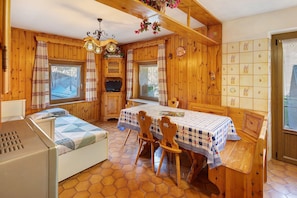 Interior acollidor d'una cabana amb decoració de fusta, taula de dinar amb cadires, un llit i un televisor.