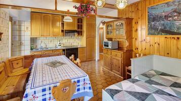 A cozy kitchen with wooden cabinets, a dining table with a checkered tablecloth, and a painting on the wall.
