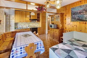 Une cuisine chaleureuse avec des meubles en bois, une table à manger recouverte d’une nappe à carreaux et un tableau accroché au mur.