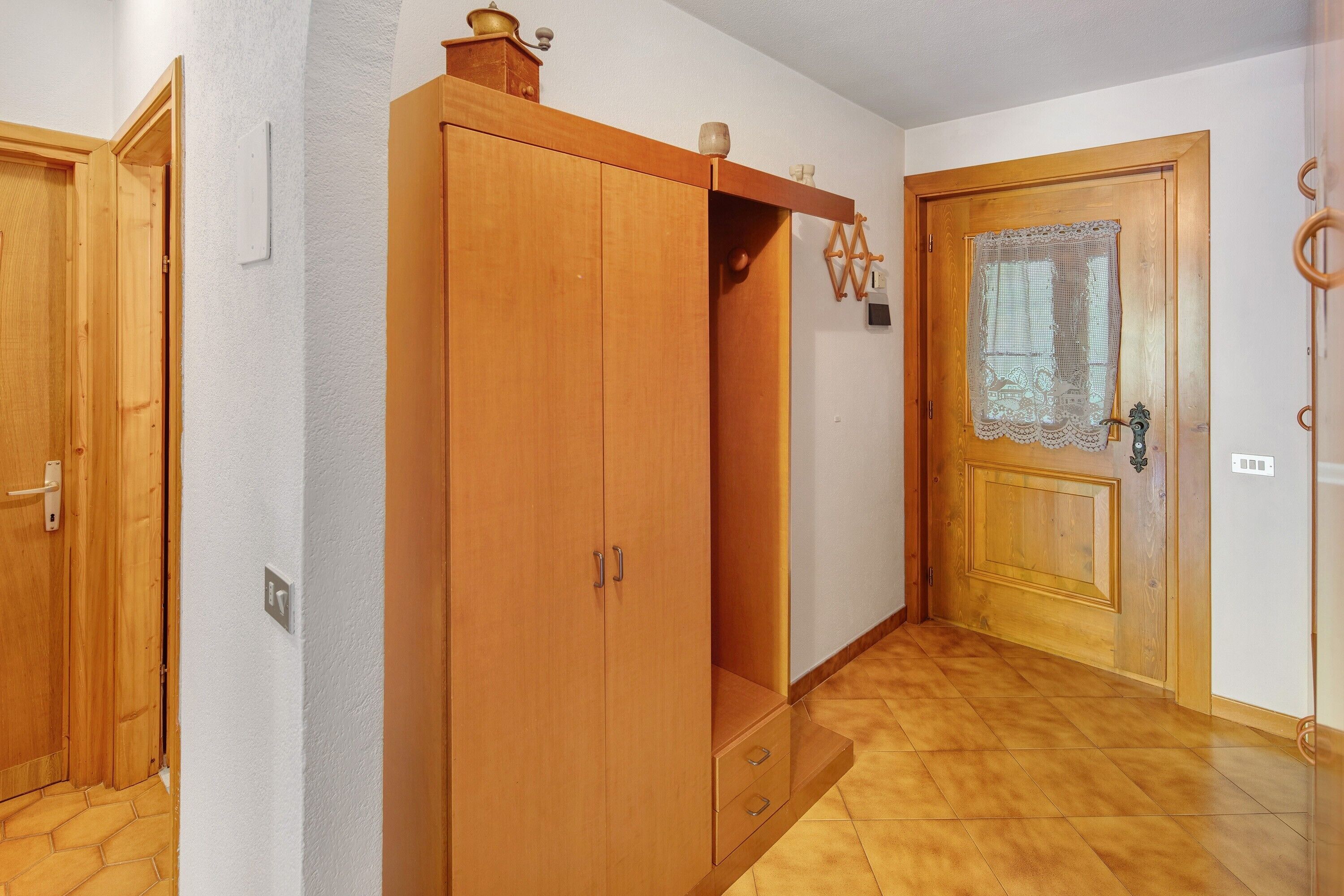A hallway with wooden doors, a wardrobe, and a tiled floor.