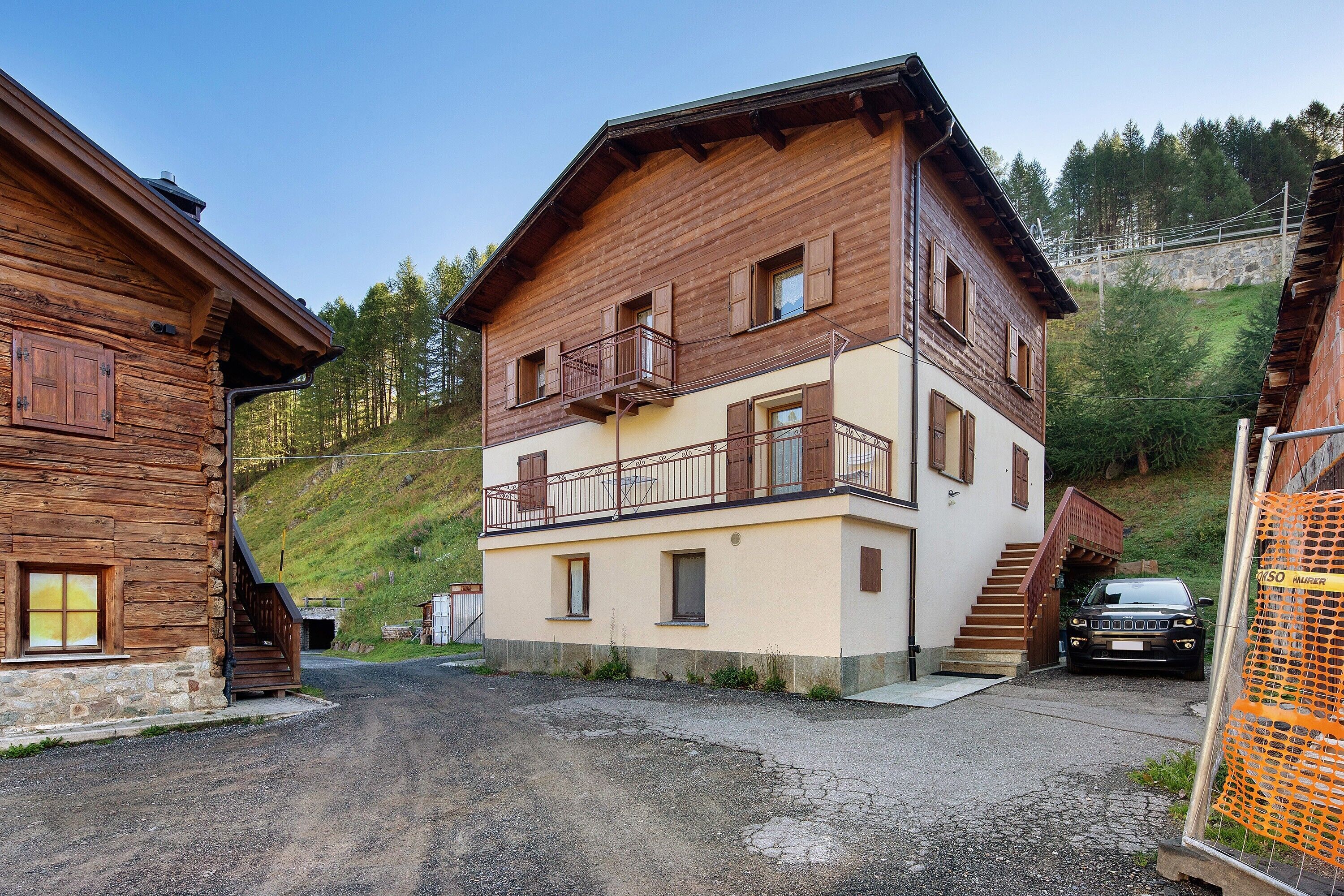 Un bâtiment en bois à deux étages, doté d’un balcon, avec une voiture garée devant.