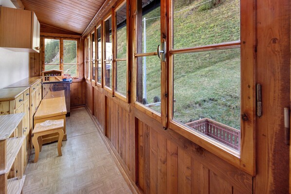 L’intérieur d’un chalet en bois comprend un coin cuisine, une table à manger et de grandes fenêtres qui offrent une vue sur une colline verdoyante.