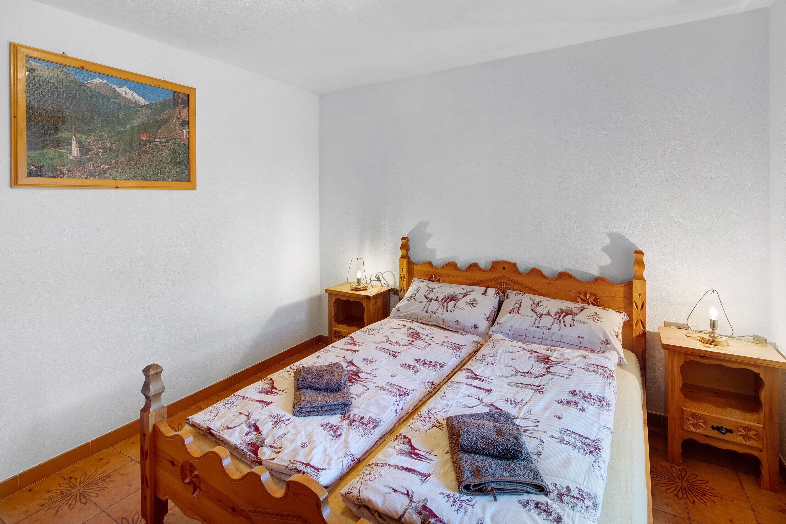 Ein Schlafzimmer mit einem hölzernen Bett, zwei Nachttischen, einem Wandbild und einer gemusterten Bettdecke.