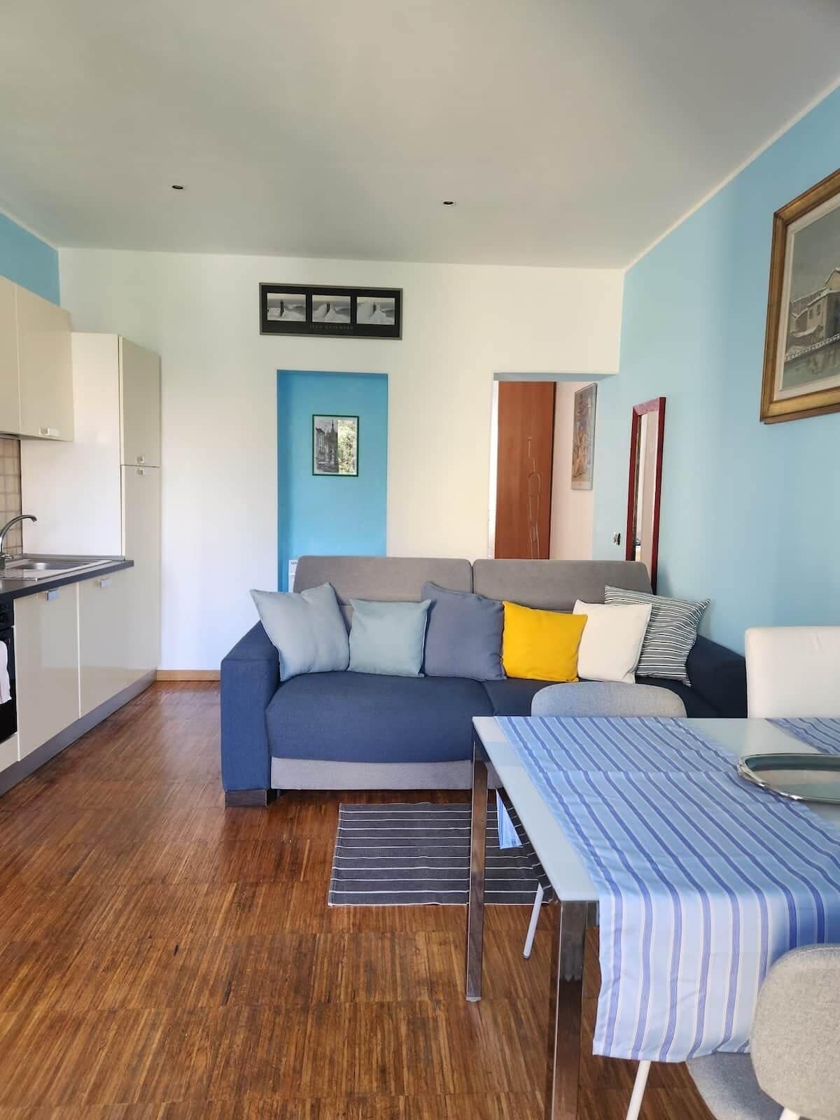 A compact living space with a kitchenette, a sofa with cushions, a dining table, and a bed.