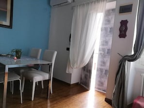 Ein Zimmer mit Esstisch, Stühlen, einer Topfpflanze und einem Vorhang.