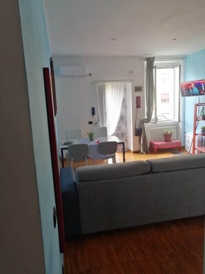 A living room with a sofa, a dining area with a table and chairs, a TV, and a window with curtains. - Locami Apartment Ca' Granda (Milan)