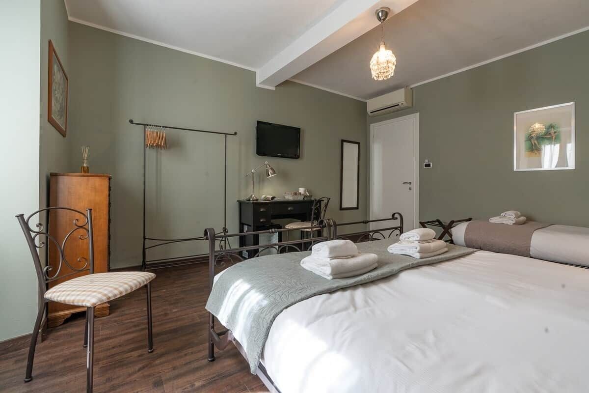 A hotel room with a bed, a desk, a chair, a television, and a chandelier.