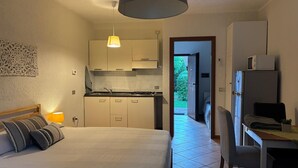 Ein Schlafzimmer mit einem Bett, einer Nachttischlampe und Blick auf eine Küche sowie einen Außenbereich.