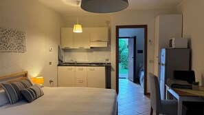Ein Schlafzimmer mit einem Bett, einer Nachttischlampe und Blick auf eine Küche sowie einen Außenbereich.