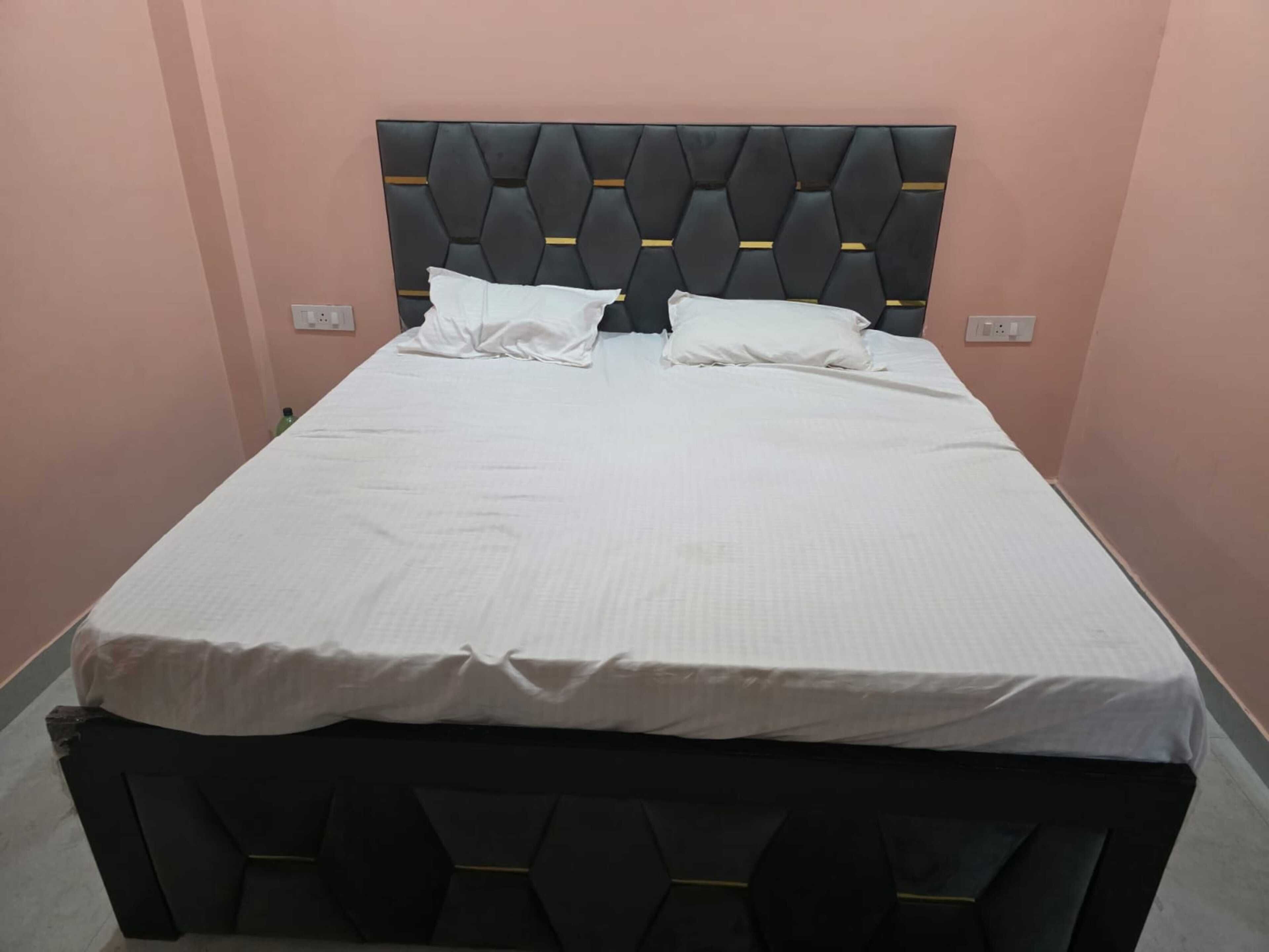 A single bed with a black upholstered headboard and white bedding in a room with pink walls.