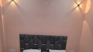 A bed with a black headboard and white bedding in a room with peach walls and wall-mounted lights.