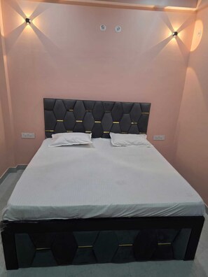 A bed with a black headboard and white bedding in a room with peach walls and wall-mounted lights.
