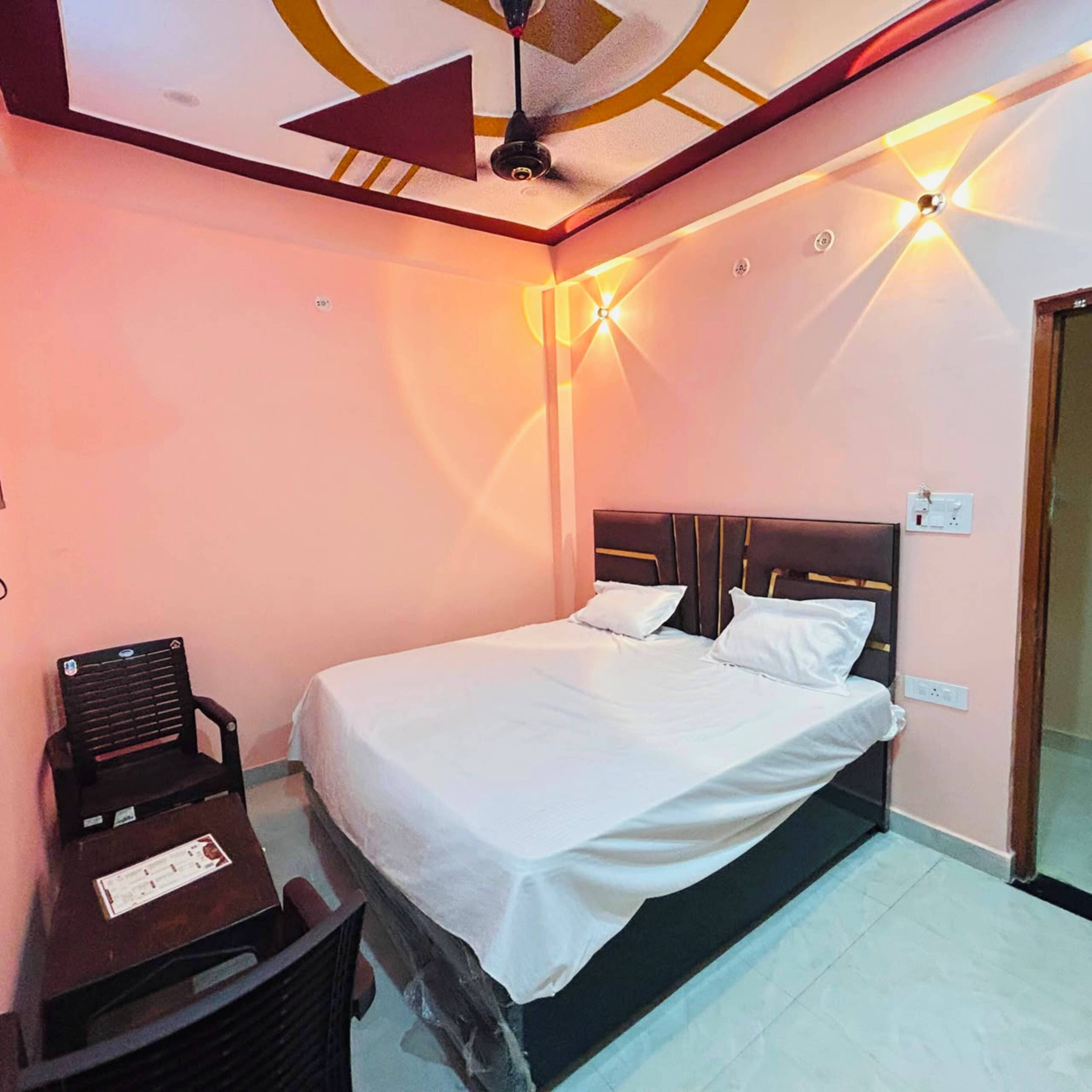 Uma cama de solteiro com cabeceira, uma escrivaninha com cadeira e um ventilador de teto em um quarto com paredes cor de rosa.