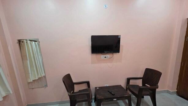 A room with a television mounted on the wall, two wooden chairs, a small table, and a curtain on the left.